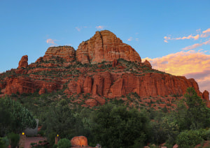Закат над красными скалами Седоны, обрамленный зелеными деревьями и ярким голубым небом с облаками.